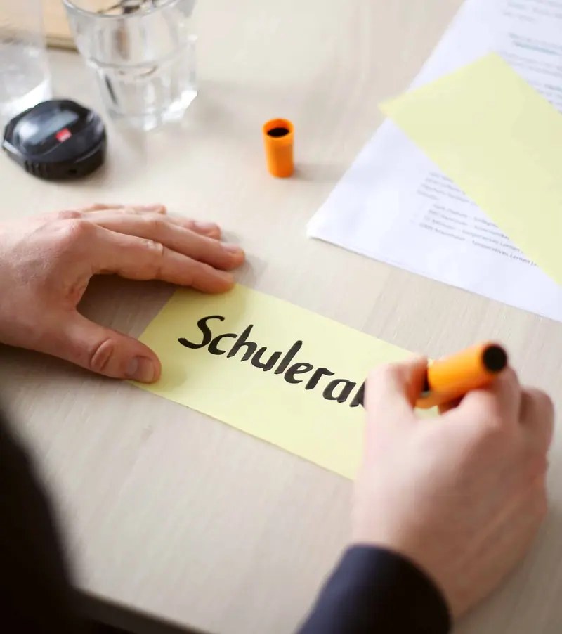 Hände beschriften eine Moderationskarte mit dem Wort Schule